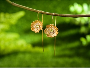 Macro view of floral silver earrings with green gemstone center on a natural branch