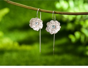 Macro shot of handmade S925 silver flower earrings with blue stone on a tree branch