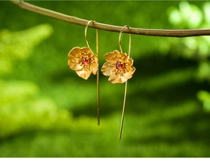 Macro shot of gold flower earrings with red garnet centers hanging on a branch