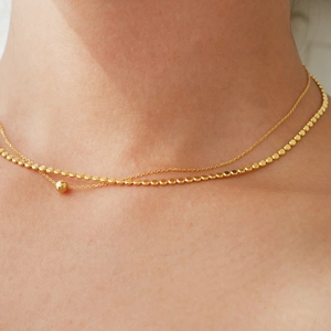 Detail of a layered 925 silver golden choker necklace featuring a delicate ball chain and bead