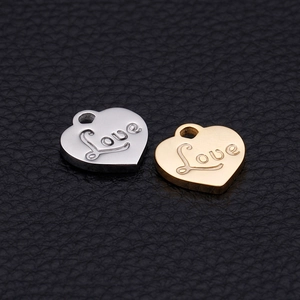 Polished gold and silver heart pendants with Love engraving on black leather surface