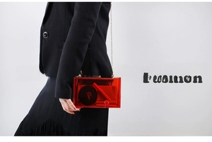 Macro detail of red acrylic evening clutch bag showing golden chain and inner capacity