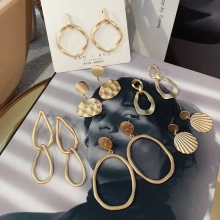 Artistic detail of gold geometric earrings featuring matte circles and teardrop charms