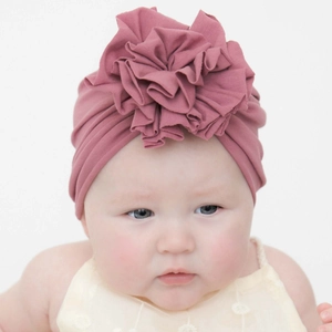 Detailed view of a soft pink knitted baby turban featuring a large ruffled flower ornament