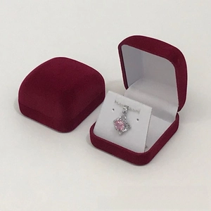 Detail of red velvet jewelry gift box showing a heart pendant necklace with pink gem