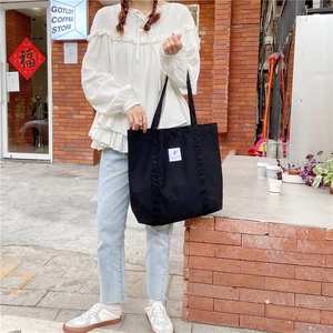 Detail of minimalist black canvas tote bag featuring double straps and white front label
