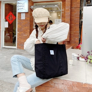 Minimalist black canvas tote bag for women shown in a stylish outdoor cafe setting