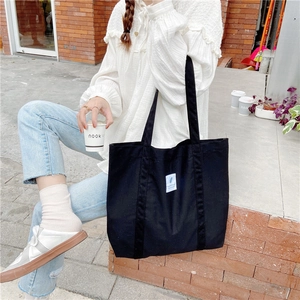 Detail view of large black canvas tote bag with white patch label and wide shoulder straps