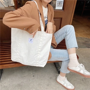 Close-up of cream canvas tote bag with retro textile label on long shoulder strap