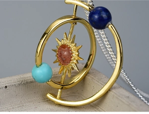 Macro shot of solar system necklace pendant with red stone and golden orbital rings