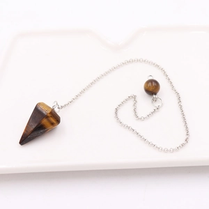 Macro shot of tiger eye crystal pendulum with silver chain on white ceramic tray