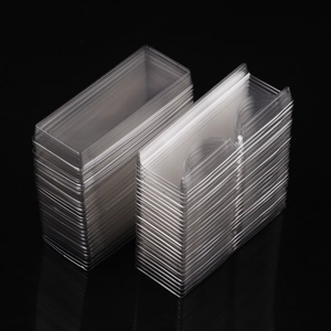 Stack of 60 clear plastic eyelash storage trays with lids on professional black background
