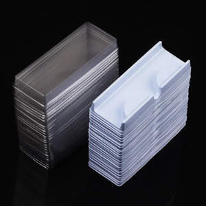 Bulk clear and white false eyelash inner trays stacked on a sleek black background