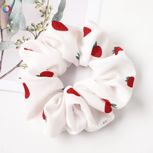 Close-up of white fabric scrunchie featuring red strawberry patterns on card