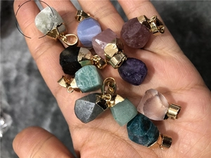 Detailed view of eleven assorted natural raw stone pendants held in hand with gold clasps
