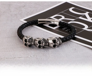 Detail of a braided black leather bracelet featuring vintage skull charms and a magnetic clasp