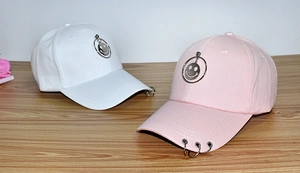 Detail of white and pink baseball caps with metal smiley face and brim ring accents