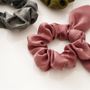 Detail view of satin hair scrunchies in pink, gray, and green with elegant silk texture