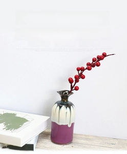 Detail of red Christmas berry branches in a ceramic vase on a wooden surface