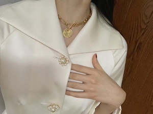 Detalle de collar con colgante de moneda de oro sobre una chaqueta blanca con perlas