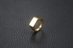 Polished gold rectangular signet ring for men on a black leather surface