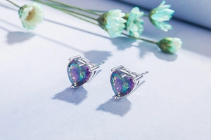 Close-up of heart-shaped rainbow opal stud earrings with faceted stones in silver setting