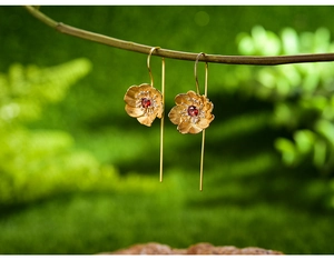 Macro shot of gold floral earrings with red garnet center hanging on green branches