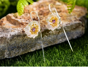 Close-up of floral silver earrings with purple gemstones on natural moss and stone