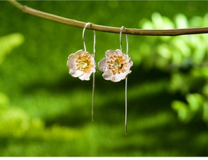 Macro detail of S925 silver flower earring with green gemstone on a natural branch