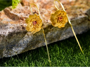 Macro detail of gold flower earrings with red garnet centers resting on a natural stone