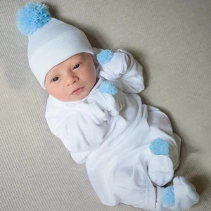Newborn baby wearing soft white knitted hat and complete outfit with light blue pom-poms