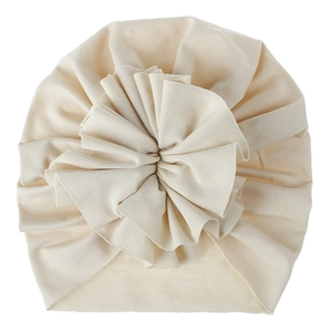 Close-up of a soft cream knitted baby turban hat with a large ruffled flower detail.
