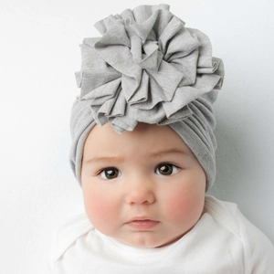 Detail of a grey baby turban hat with a large ruffled flower on a cute infant model.