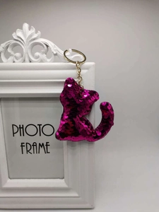 Close-up of rose red sequin cat keychain with golden ring on a white vintage frame