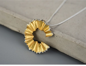Macro shot of pencil shaving pendant in gold and silver finish on stone texture