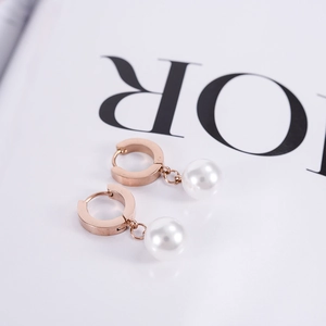 Détail de créoles en or rose avec pendentifs en perles blanches sur fond de magazine blanc