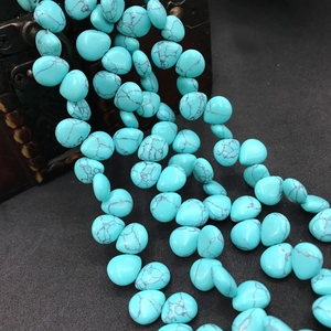 Close-up of green turquoise teardrop beads with black marble patterns on dark wood