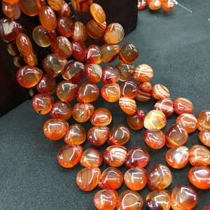 Macro detail of orange agate beads with white stripes spilling from a dark bowl