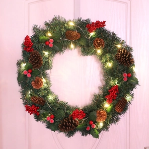 Christmas wreath with red berries, pine cones and warm LED lights on a door decor
