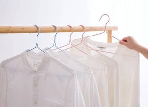 Detail of non-slip plastic coated hangers in pink and blue on a wooden clothes rail