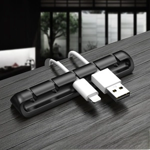 Close-up of black 5-slot silicone cable organizer managing white USB cords on a wooden desk
