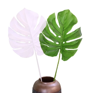 Artificial monstera leaves in green and white colors with brown ceramic vase