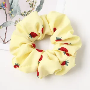 Detailed view of a yellow scrunchie with red strawberry print and soft pleated texture