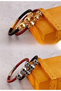 Detail of woven leather bracelets with metallic skull charms in gold and silver finish