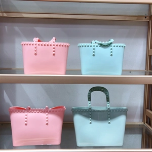 Detail of studded jelly tote bags in pink and mint green on a glass shelf display