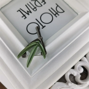 Detailed close-up of green bamboo leaf brooch with vintage metallic finish on a frame
