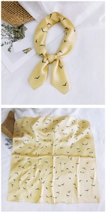 Detail of yellow silk scarf featuring black bird print and smooth satin texture