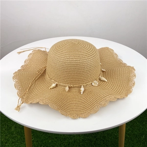 Chapeau de paille kaki à large bord ondulé avec décorations de coquillages sur table