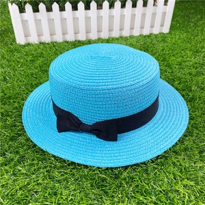 Detailed top view of blue straw boater hat with black ribbon bow on green grass