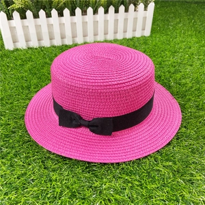 Close-up of pink woven straw hat featuring a chic black bow ribbon on artificial lawn